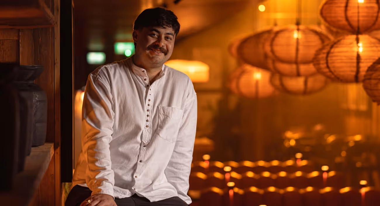 Chef in a white shirt seated in a candlelit dining room hung with paper lanterns