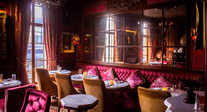 Magenta velvet banquettes and gilt-framed portraits by tall windows at Peruke & Periwig