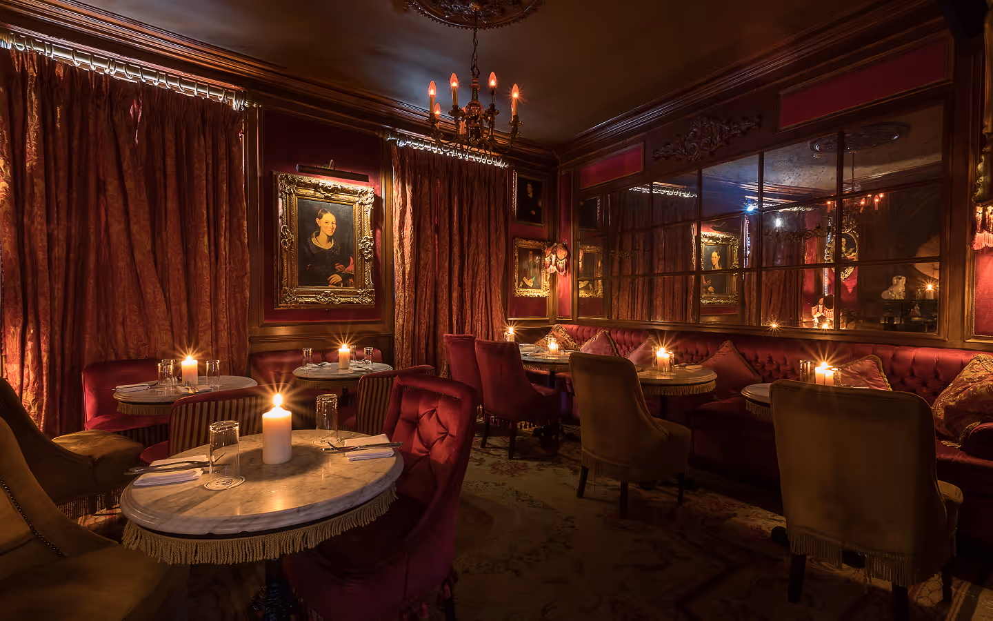 Candlelit salon with red velvet seating, marble tables and gilt-framed portraits at Peruke & Periwig