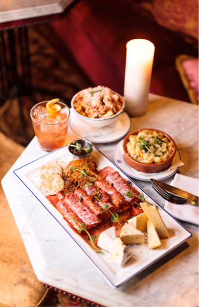 Charcuterie and cheese board with small plates and a cocktail on a marble table at Peruke & Periwig