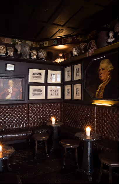 Buttoned leather banquettes and candlelit tables beneath portraits and wig busts at Peruke & Periwig