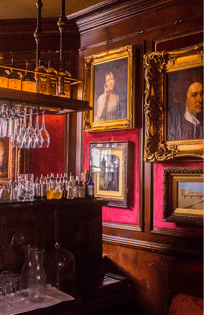 Gilt-framed portraits on a red velvet wall beside the mahogany bar at Peruke & Periwig
