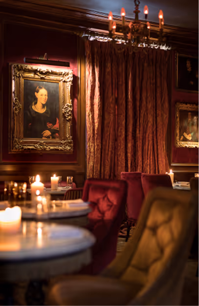 Velvet armchairs and candlelit marble tables beneath a gilt-framed portrait at Peruke & Periwig