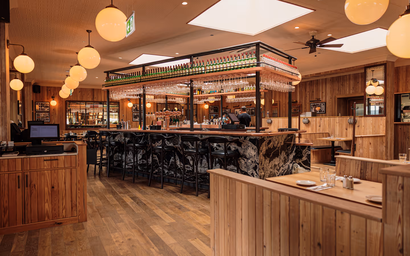 Marble-fronted island bar with stools and globe pendant lights in the timber-clad room at Elephant & Castle
