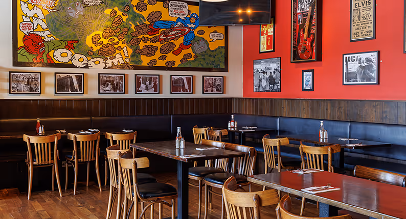 Comic-book mural and framed rock memorabilia above banquette seating at Captain Americas
