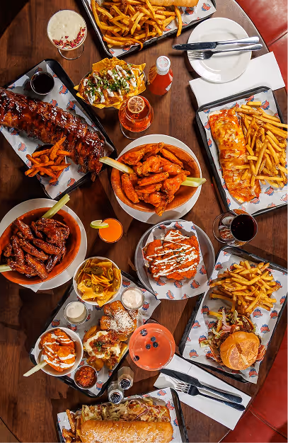 Overhead spread of ribs, buffalo wings, loaded fries and burgers on a wooden table at Captain Americas