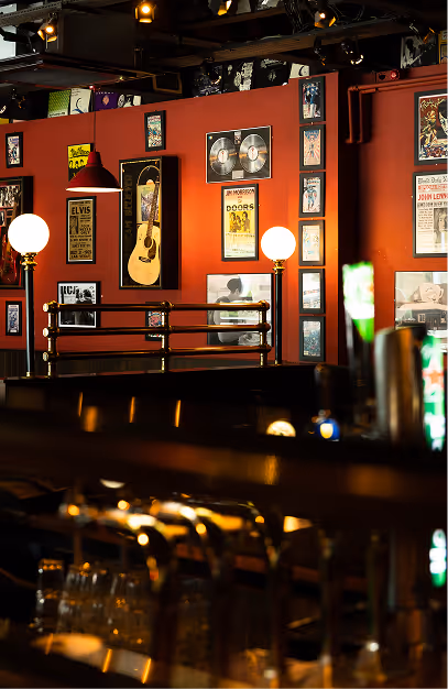 Red wall of framed music memorabilia, gold discs and a mounted guitar above the bar at Captain Americas