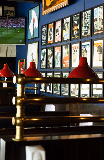 Framed magazine covers, red pendant lamps and brass-railed booths beside a sports screen at Captain Americas