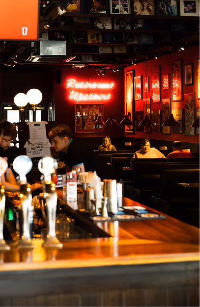 Bar taps and booth seating beneath a red neon restrooms sign at Captain Americas