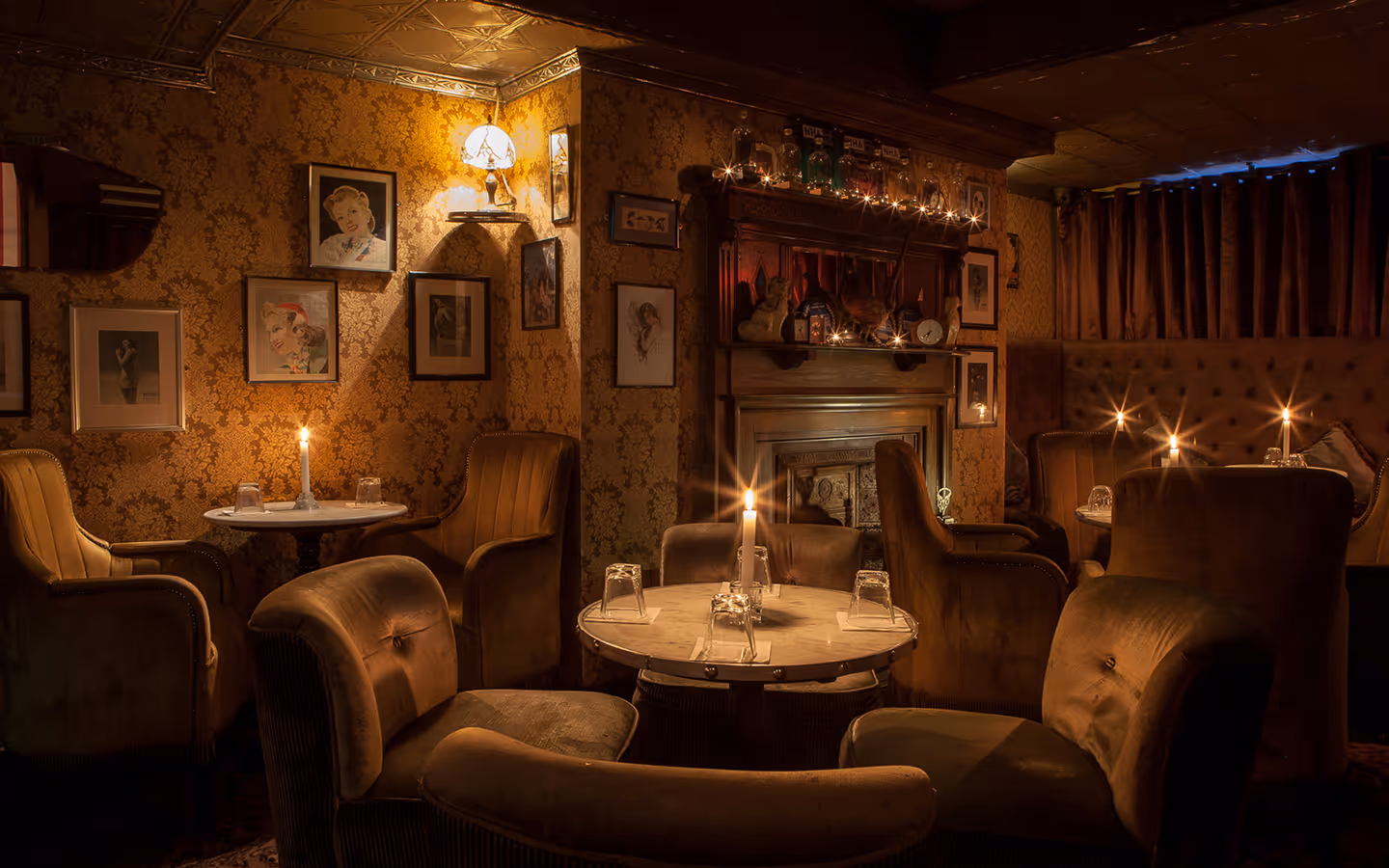 Candlelit marble tables and velvet armchairs beneath a wall of framed portraits at Vintage Cocktail Club
