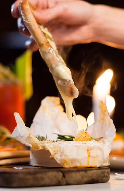 Hand dipping bread into a molten baked camembert on a wooden board at Vintage Cocktail Club