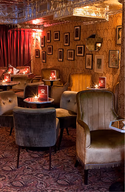 Velvet armchairs and candlelit tables with red menus below a gallery wall at Vintage Cocktail Club