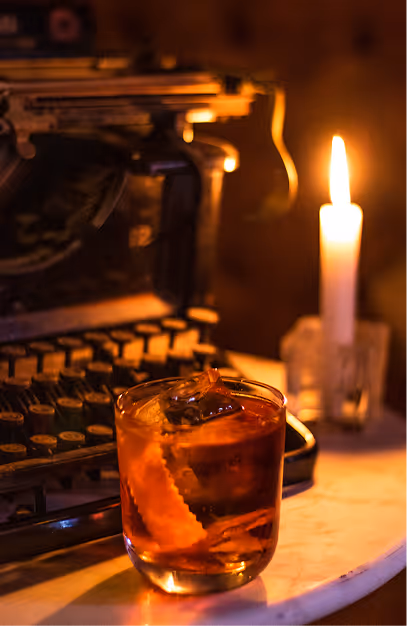 Amber cocktail with an orange twist beside an antique typewriter and candle at Vintage Cocktail Club