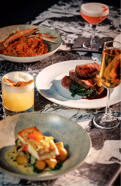 Langoustine linguine, sliced steak and white fish with cocktails on a marble table at The Grayson