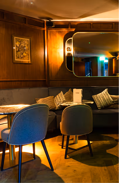 Grey banquette and upholstered chairs beneath a brass-framed mirror in the wood-panelled bar at The Grayson