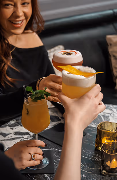 Guests raising garnished cocktails over a marble table at The Grayson