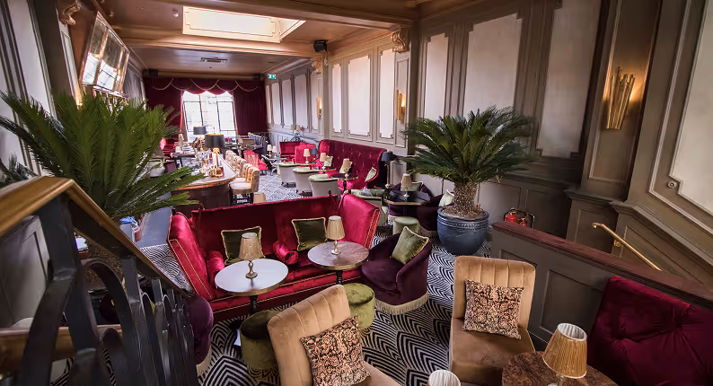 Crimson velvet banquettes and palms on a chevron rug in the lounge at Stella Cocktail Club