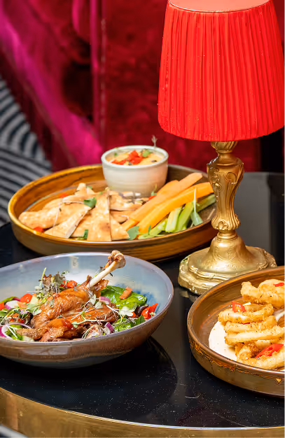 Sharing plates of flatbread, crudites and calamari beside a red table lamp at Stella Cocktail Club