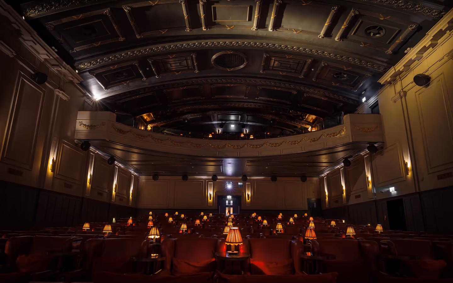 Art deco auditorium with red velvet armchairs and lamp-lit tables at Stella Cinema