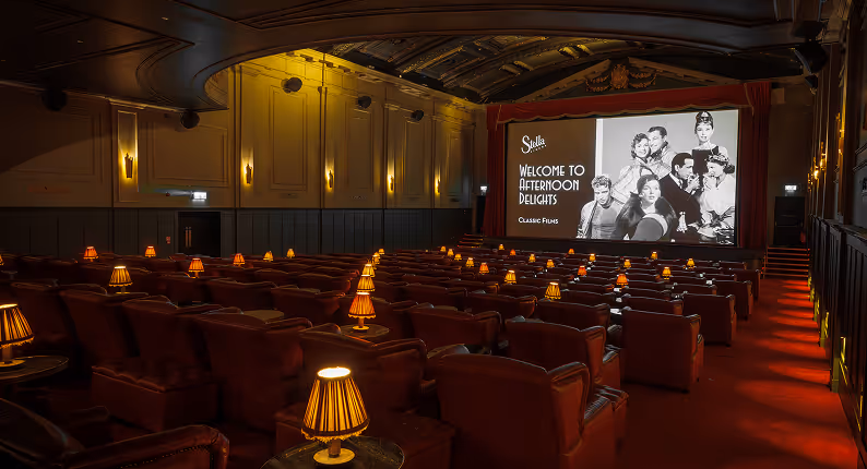 Stella Cinema auditorium with red velvet seats, warm lighting and a large screen showing a vintage film presentation.