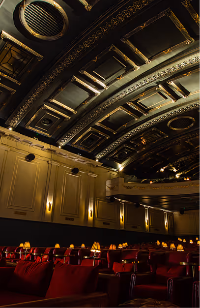 Gilded barrel-vaulted ceiling above red velvet seating and wall sconces at Stella Cinema
