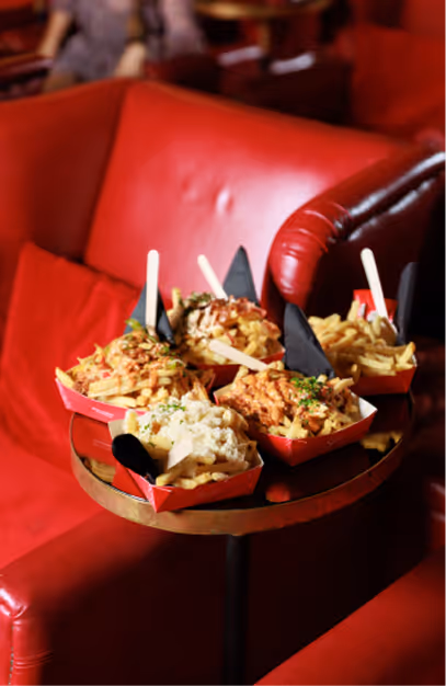 Loaded fries in red trays on a brass table beside red leather seating at Stella Cinema