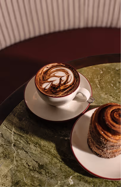 Latte art coffee and a swirled cinnamon pastry on green marble at Amelia's Table