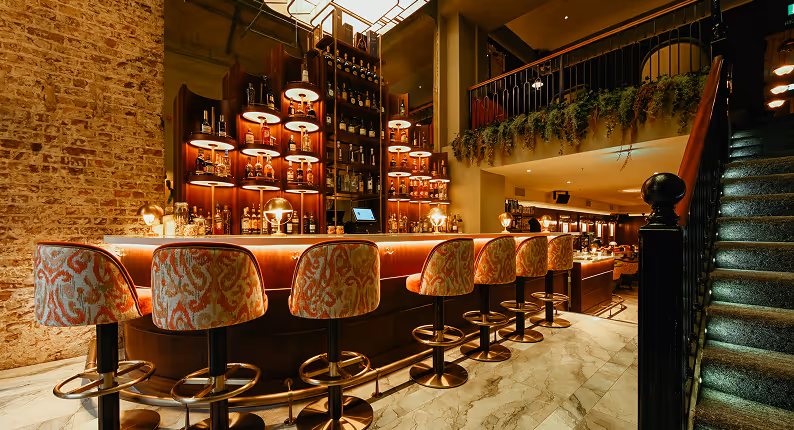 Curved bar with patterned stools and backlit spirits against exposed brick at The Stapleton