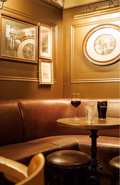 Curved leather banquette and marble table with wine, a highball and a pint at The Stapleton