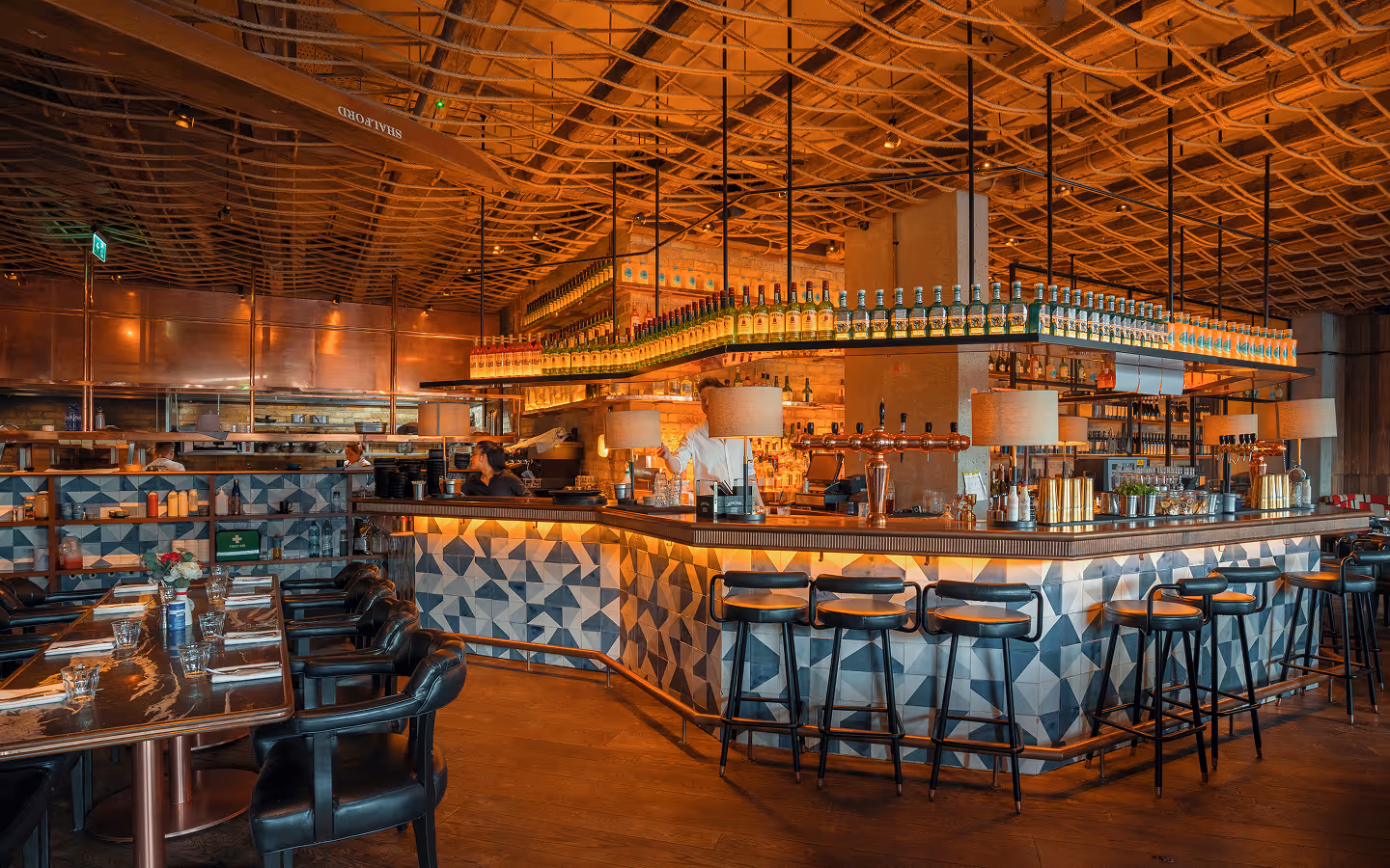 Geometric tiled bar counter with stools and backlit spirits shelves at Mackenzie's