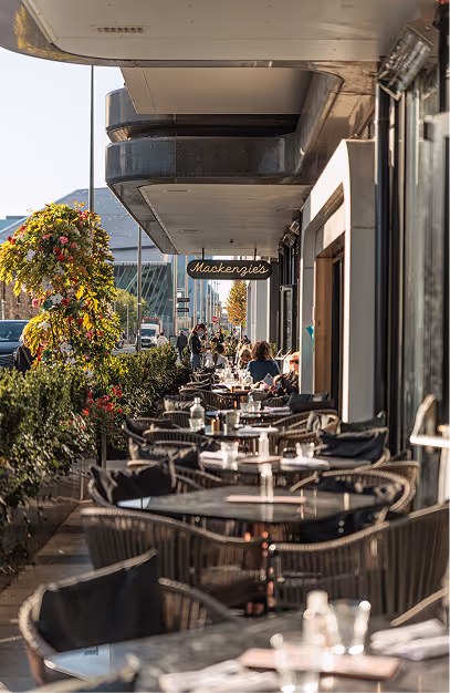 Outdoor terrace with rattan chairs and hanging flower baskets beneath the Mackenzie's sign