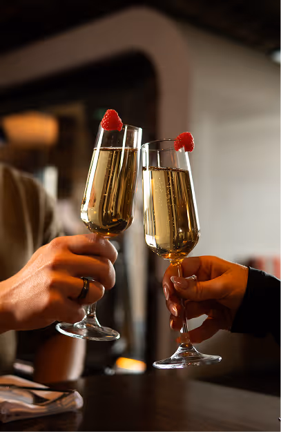 Two hands toasting sparkling wine flutes garnished with raspberries at Mackenzie's