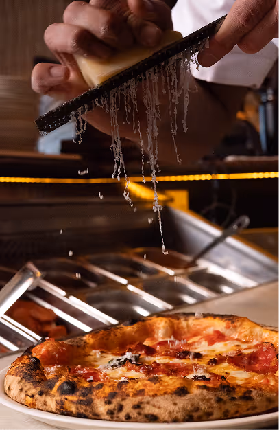 Chef grating cheese over a freshly baked pizza in the kitchen at Mackenzie's