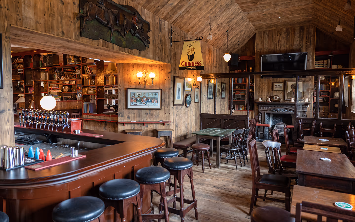 Curved timber bar, leather stools and open fireplace in the wood-panelled pub at Foxhunter