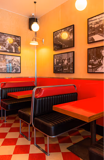 Red and black diner booths on a checkerboard floor beneath black-and-white photographs at Wowburger