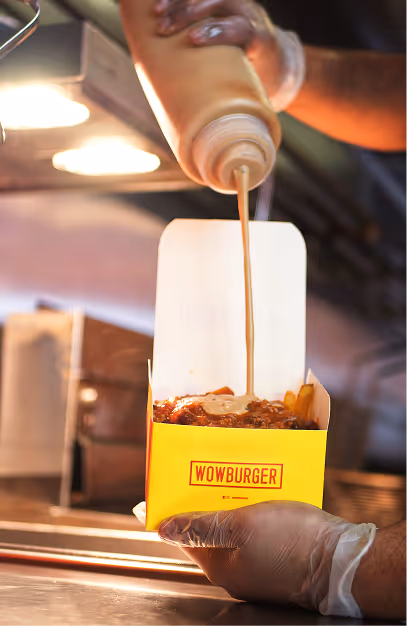 Sauce poured over loaded fries in a Wowburger carton at the kitchen pass