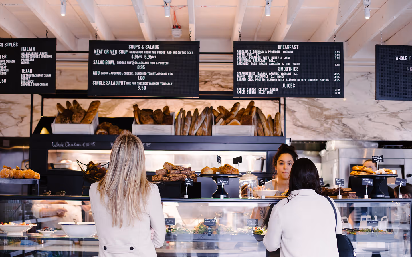 Customers at the bakery and salad counter under menu boards at Angelina's Deli