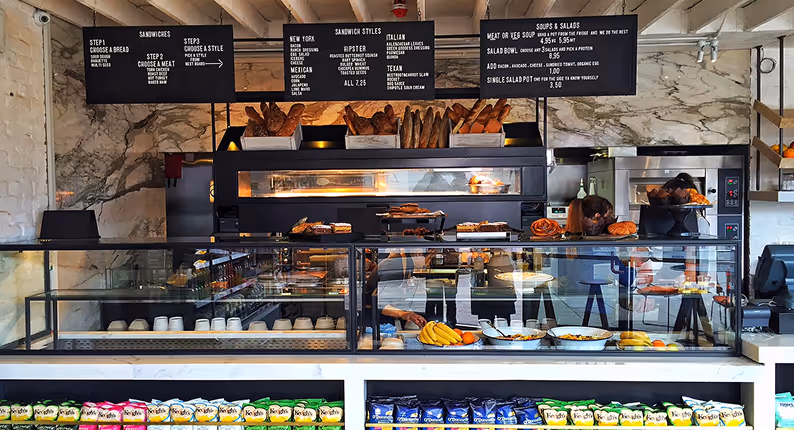 Deli counter with sandwich menu boards, fresh bread baskets and a glass display case at Angelina's Deli