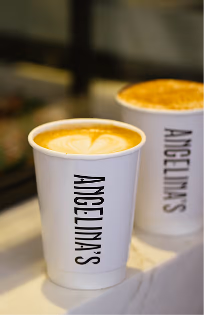 Two branded Angelina's takeaway coffee cups, one with latte art, on a marble counter