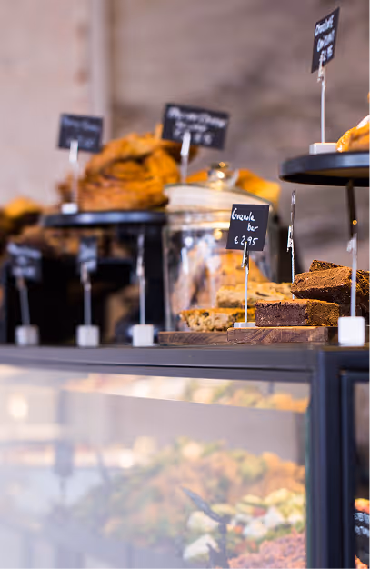Pastries and granola bars on cake stands with chalkboard price tags above the salad counter at Angelina's Deli