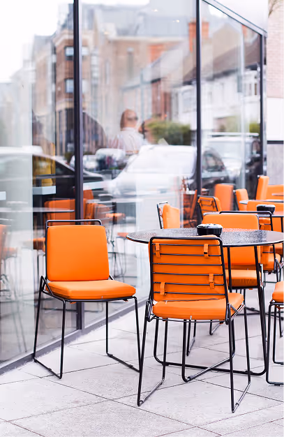 Orange pavement chairs and round tables outside the glass frontage at Angelina's Deli