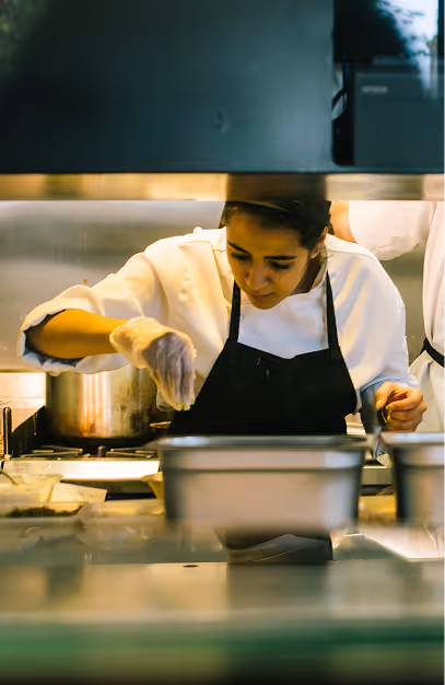 Chef in whites and a black apron plating food behind the counter at Angelina's Deli