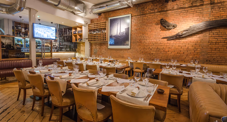 Set tables and tan leather chairs against exposed brick in the dining room at Fade St. Social