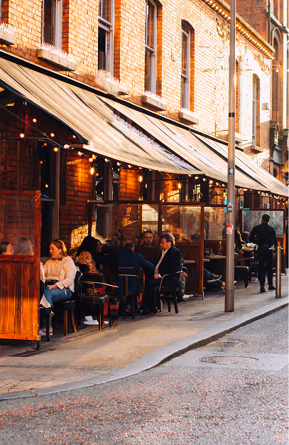 Guests on the awning-covered street terrace under festoon lights at Fade St. Social
