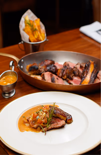 Sliced steak in a copper pan with fries and a plated steak in sauce at Fade St. Social