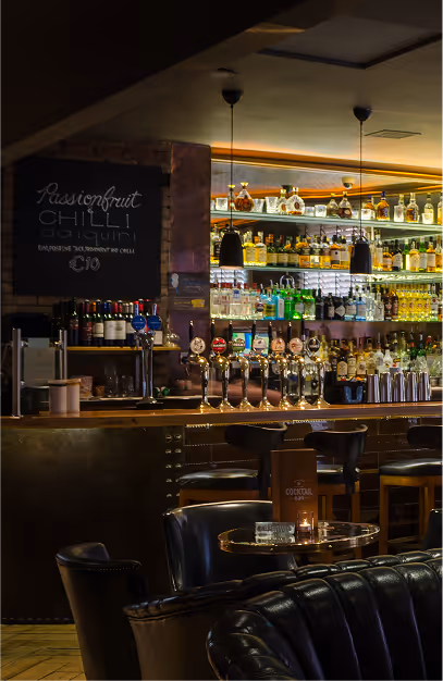 Backlit spirits shelves, brass taps and a cocktail chalkboard behind the bar at Fade St. Social