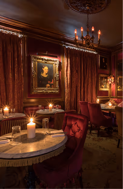 Candlelit marble tables and red velvet chairs beneath gilt-framed portraits at Peruke & Periwig