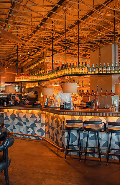 Geometric tiled bar counter with stools and backlit spirits shelf at Mackenzie's