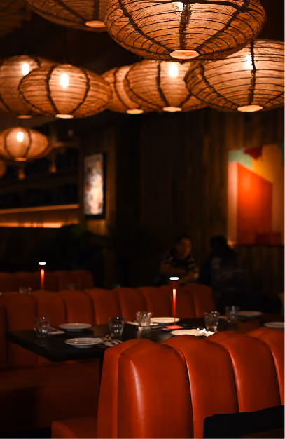 Woven globe pendant lights over orange leather banquettes and candlelit tables at Kaldero