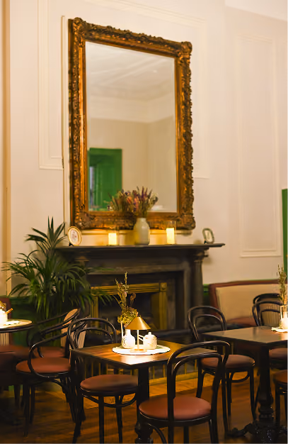 Gilt mirror above a marble fireplace with bentwood chairs and set tables at Amelia's Table